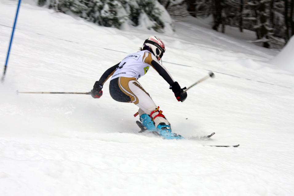 Skifahrer in voller Fahrt bei einem Wettkampf, mit Skistöcken auf einer verschneiten Piste.